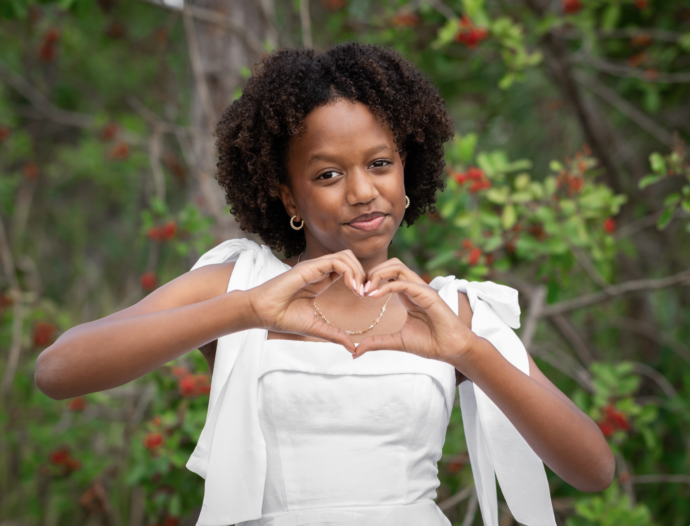 Payton making a heart with her hands, smiling outdoors